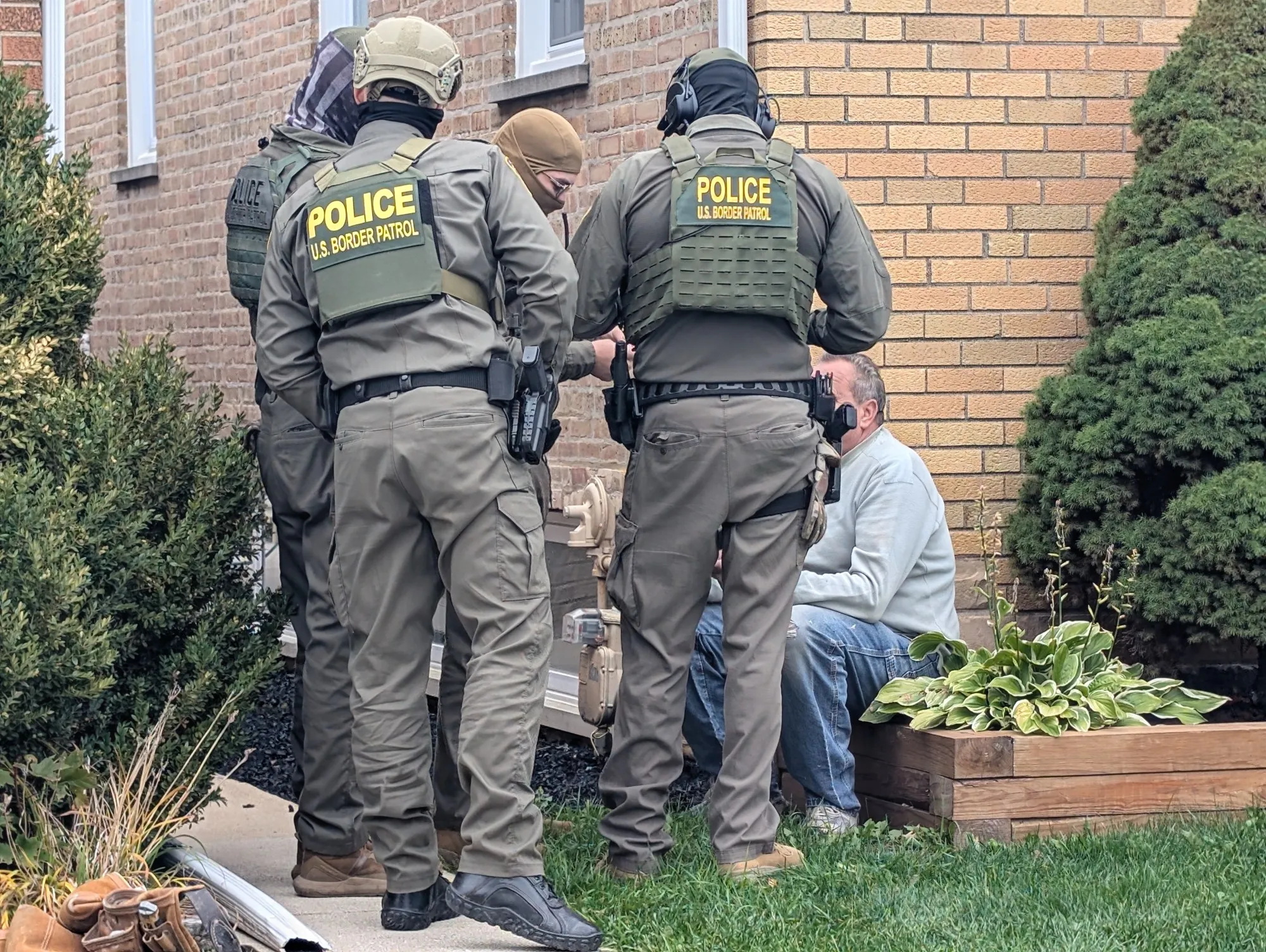 Photograph from the Edison Park scene: federal agents in tactical gear stand near a residential street, with neighbors visible in the background.
